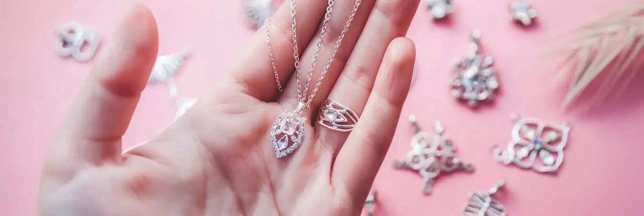 A delicate feminine hand holding a sparkling silver necklace.